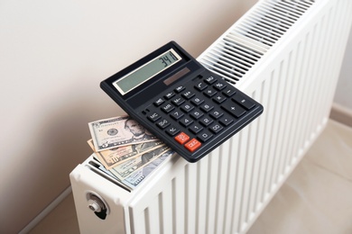 Calculator and money on heating radiator indoors