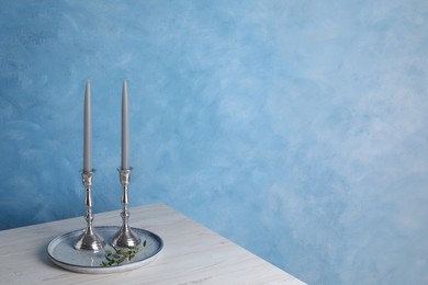 Holders with candles on wooden table near light blue wall, space for text