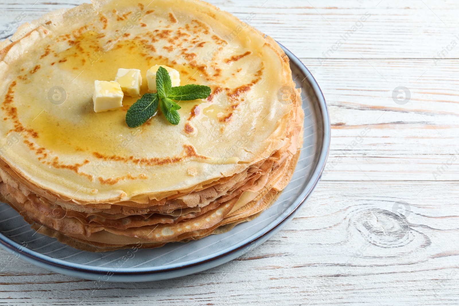 Photo of Stack of delicious crepes with mint and melting butter on white wooden table, closeup