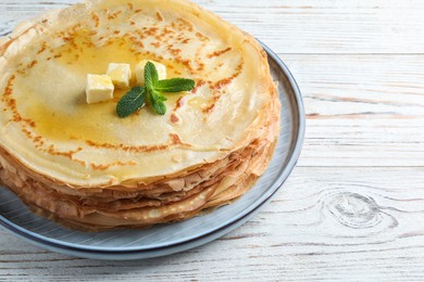 Photo of Stack of delicious crepes with mint and melting butter on white wooden table, closeup