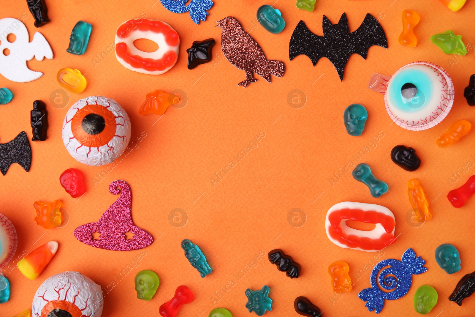 Photo of Frame made of tasty candies and Halloween decorations on orange background, flat lay. Space for text