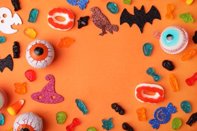 Photo of Frame made of tasty candies and Halloween decorations on orange background, flat lay. Space for text