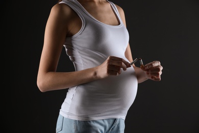 Young pregnant woman breaking cigarette on black background, closeup