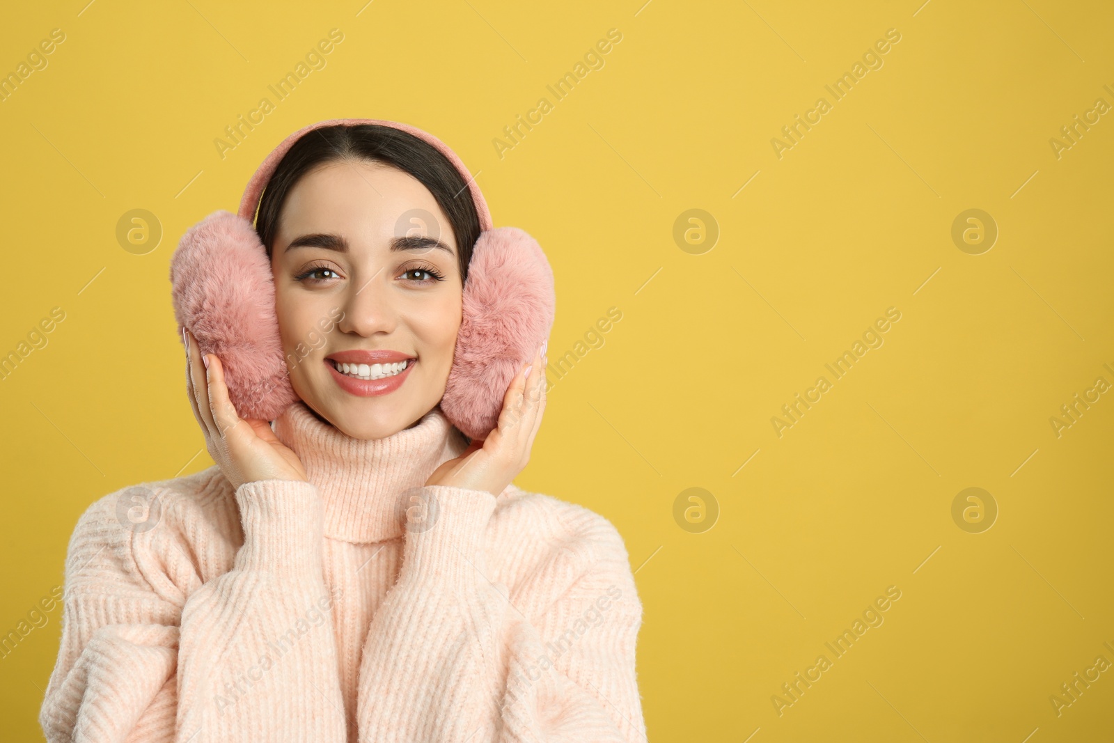 Photo of Beautiful young woman wearing earmuffs on yellow background. Space for text