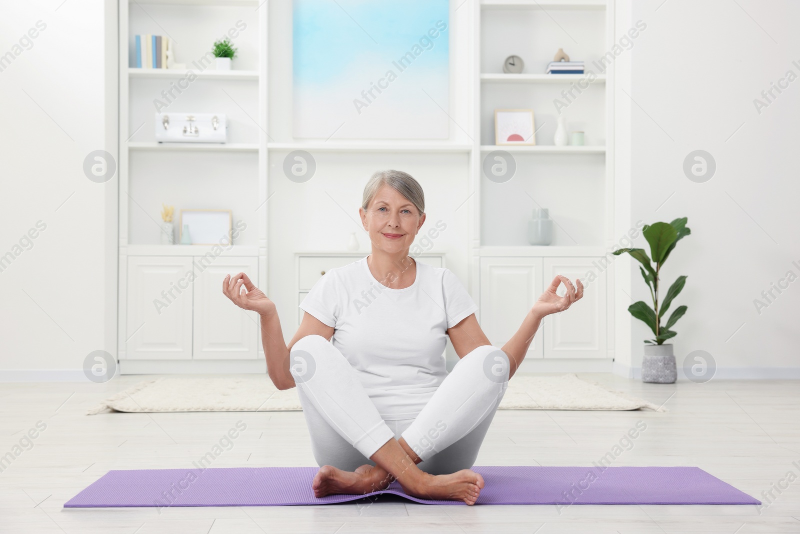 Photo of Happy senior woman practicing yoga on mat at home