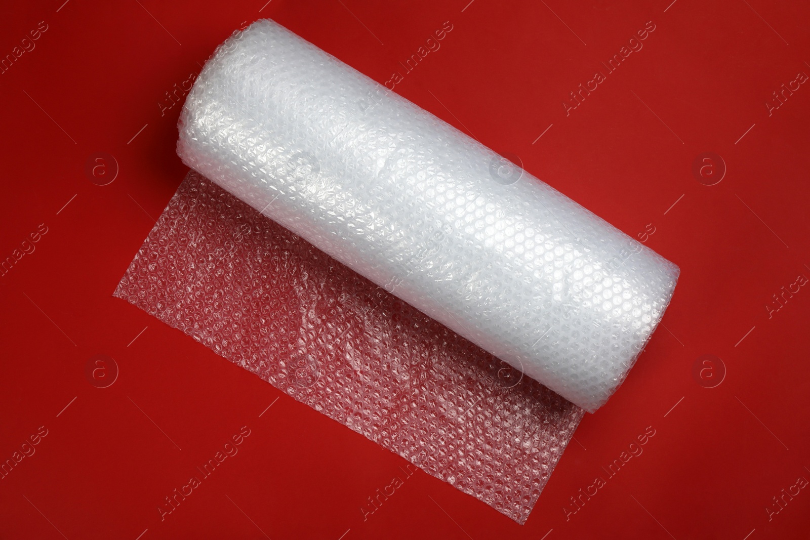 Photo of Bubble wrap roll on red background, top view