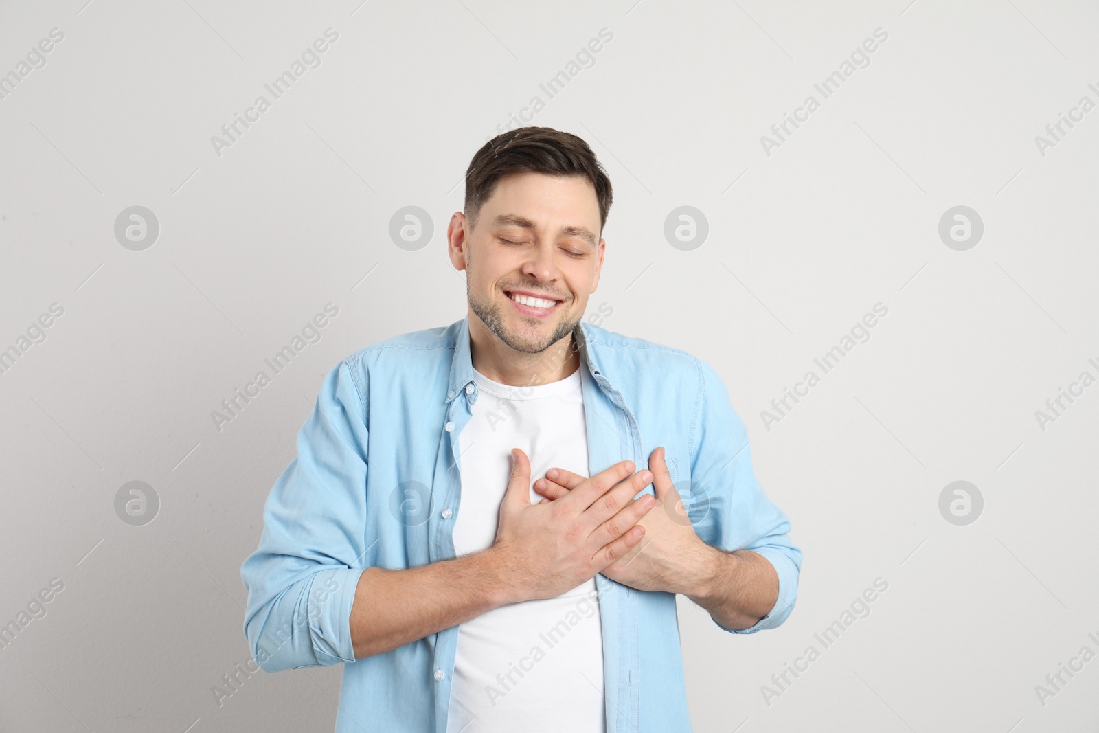 Photo of Portrait of man holding hands near heart on light background