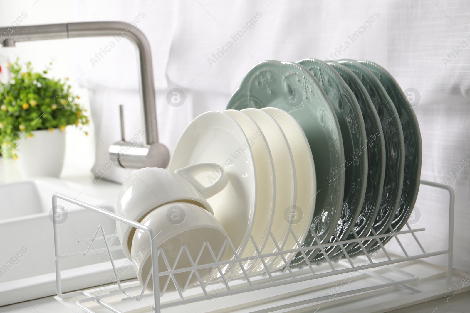 Photo of Drainer with different clean dishware and cups on white table in kitchen