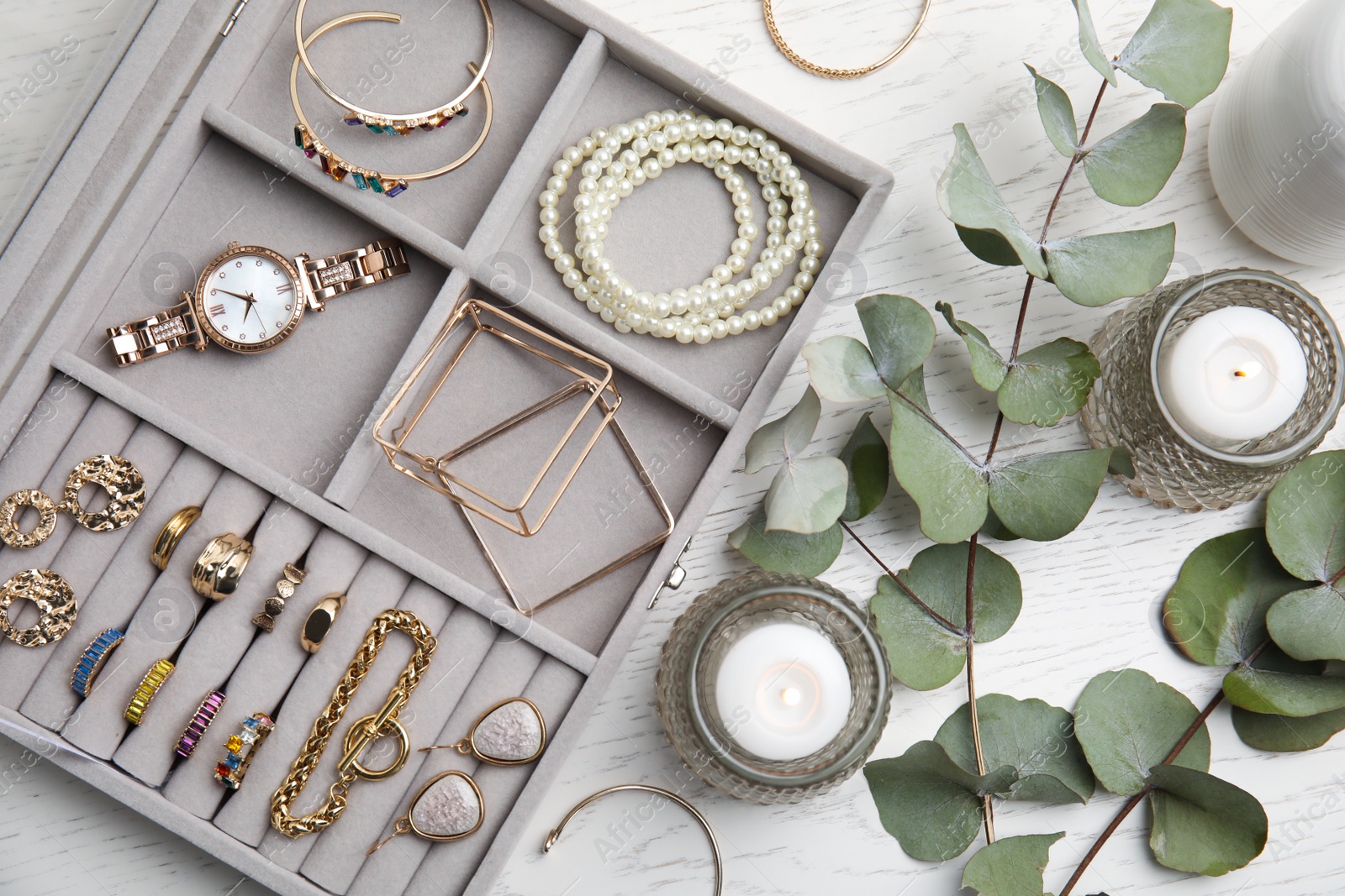 Photo of Elegant jewelry box with beautiful bijouterie and burning candles on white wooden table, flat lay