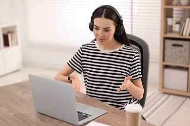 Young woman in headphones using video chat during webinar at table in room