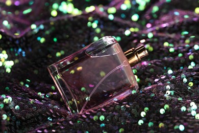 Photo of Luxury perfume in bottle on fabric with colorful sequins, closeup