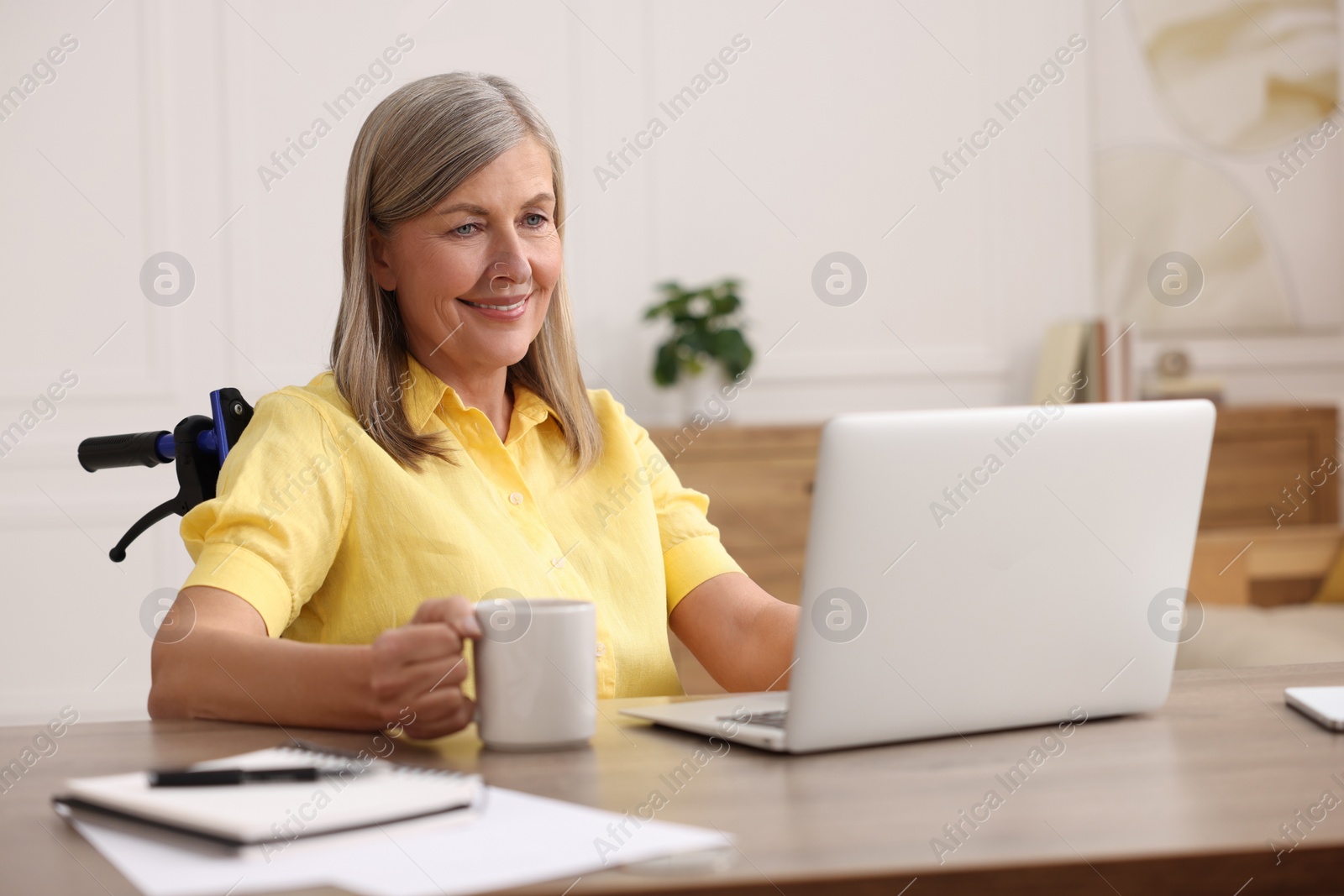 Photo of Woman in wheelchair with cup of drink using laptop at home