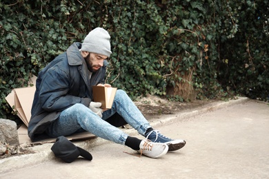 Photo of Poor homeless man with book on street in city