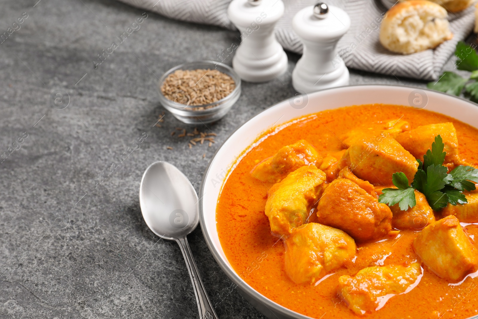 Photo of Bowl of delicious chicken curry on grey table, space for text