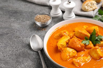 Bowl of delicious chicken curry on grey table, space for text