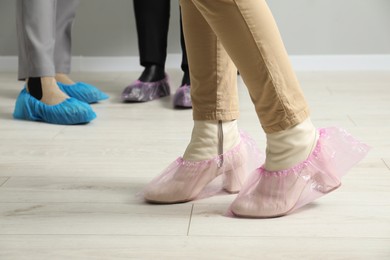 Photo of Women wearing pink shoe covers onto different footwear indoors, selective focus