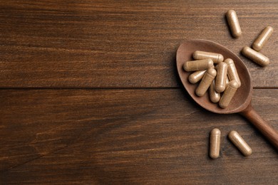 Dietary supplement capsules with spoon on wooden table, flat lay. Space for text