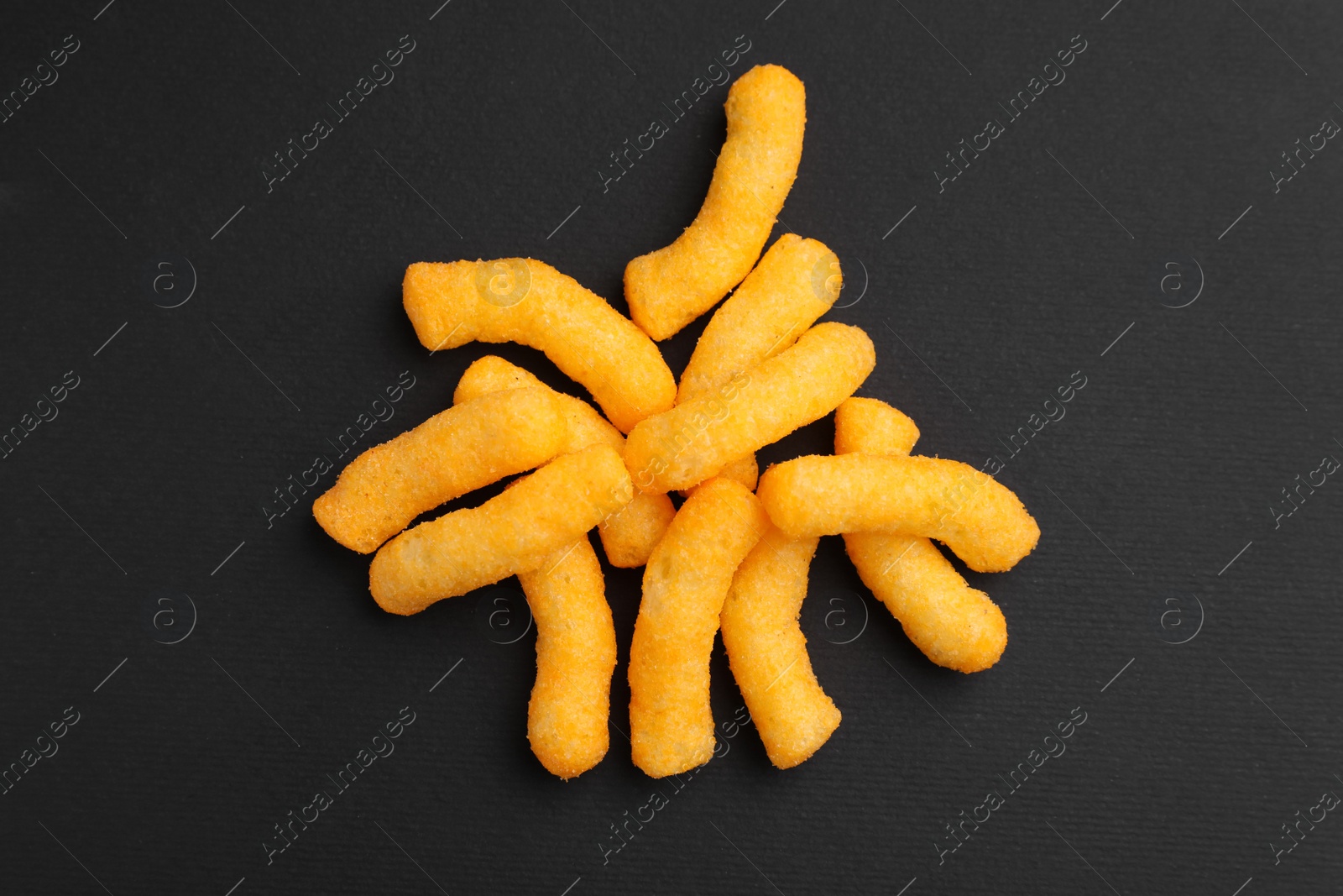 Photo of Many tasty cheesy corn puffs on black table, flat lay