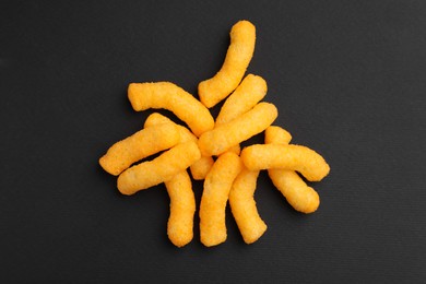 Photo of Many tasty cheesy corn puffs on black table, flat lay