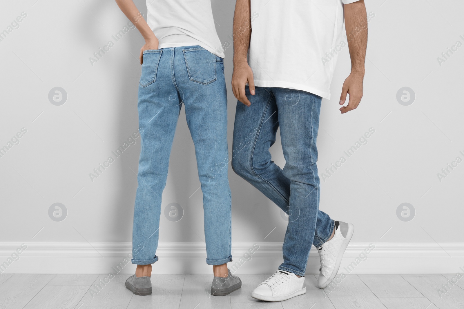 Photo of Couple in stylish jeans near light wall, closeup