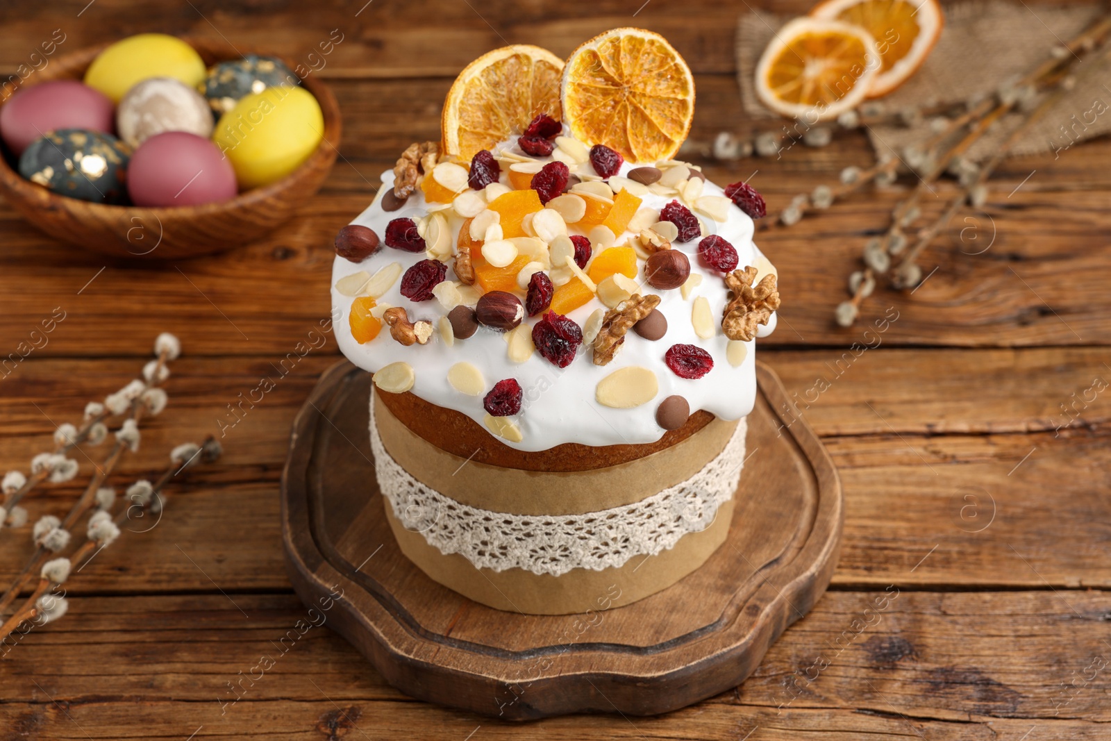 Photo of Delicious Easter cake with dried fruits, willow branches and painted eggs on wooden table