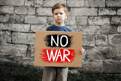 Photo of Sad boy holding poster with words No War against brick wall outdoors