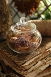 Photo of Dry roses, old book and spool of thread on table indoors, closeup