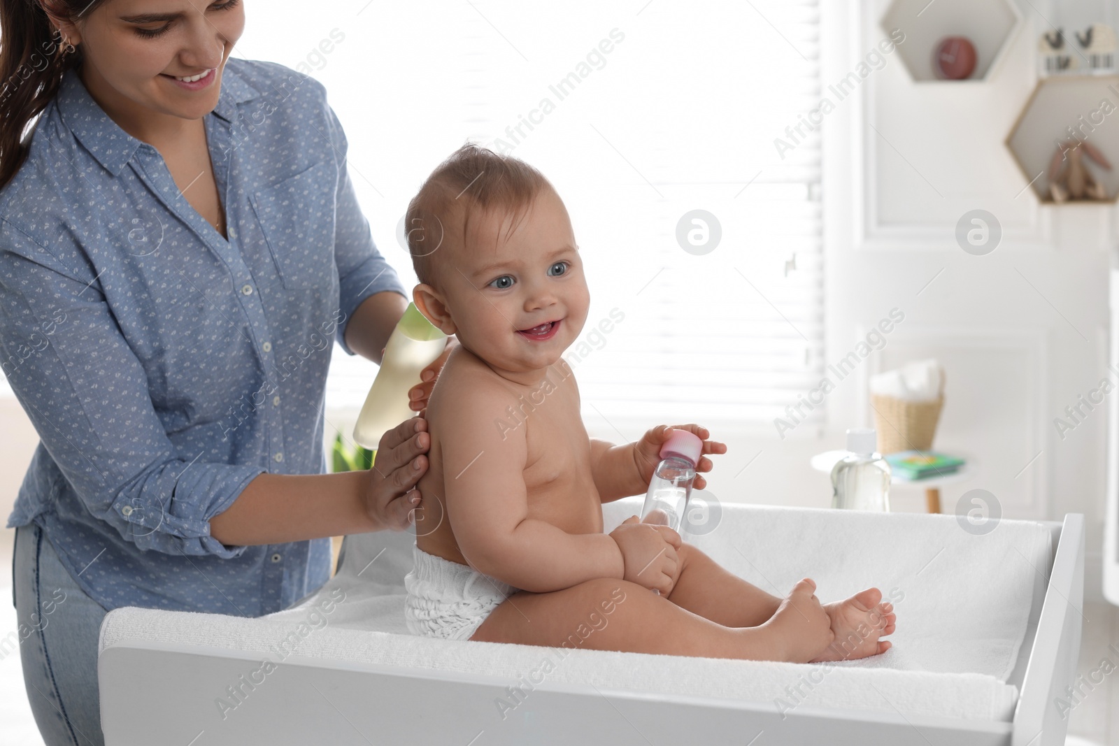 Photo of Mother massaging her cute baby with oil on changing table at home