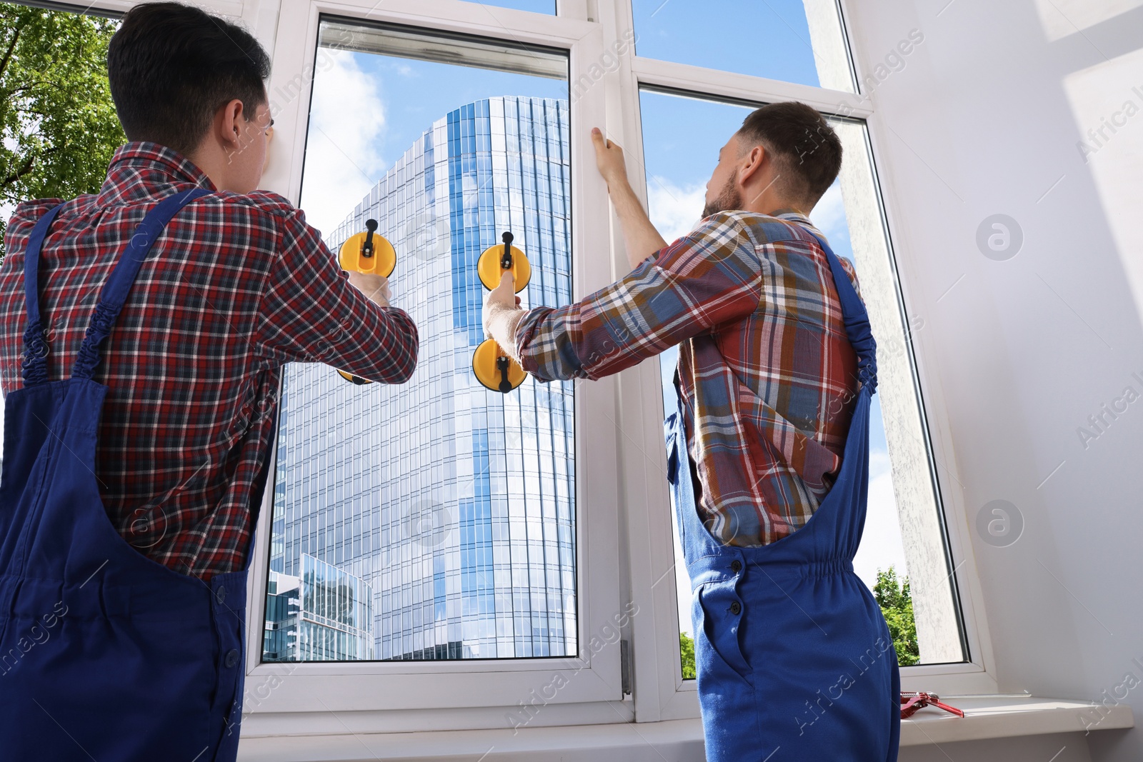 Photo of Workers using suction lifters during plastic window installation indoors