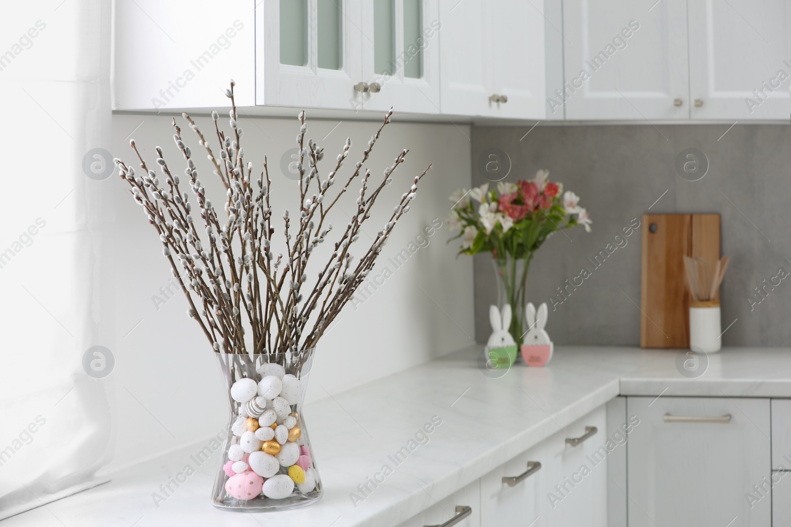 Photo of Vase with beautiful pussy willow branches and painted eggs on countertop in kitchen. Easter decor