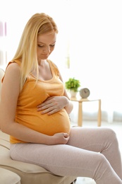 Photo of Beautiful pregnant woman sitting in light room at home