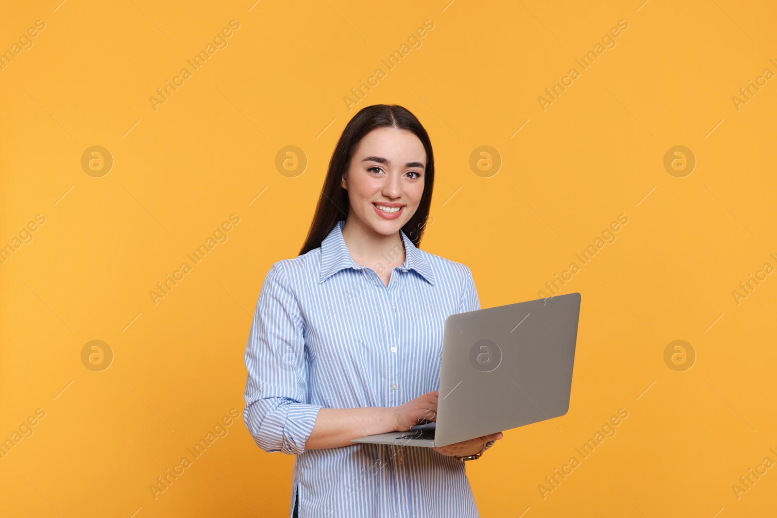 Photo of Smiling young woman with laptop on yellow background