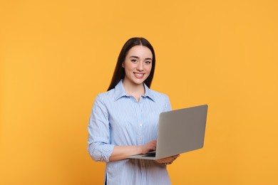 Smiling young woman with laptop on yellow background