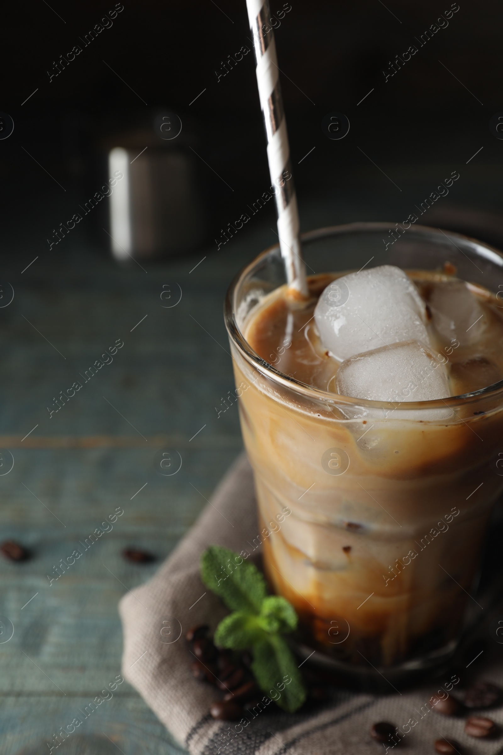 Photo of Glass of delicious iced coffee with milk, beans and mint on light blue table