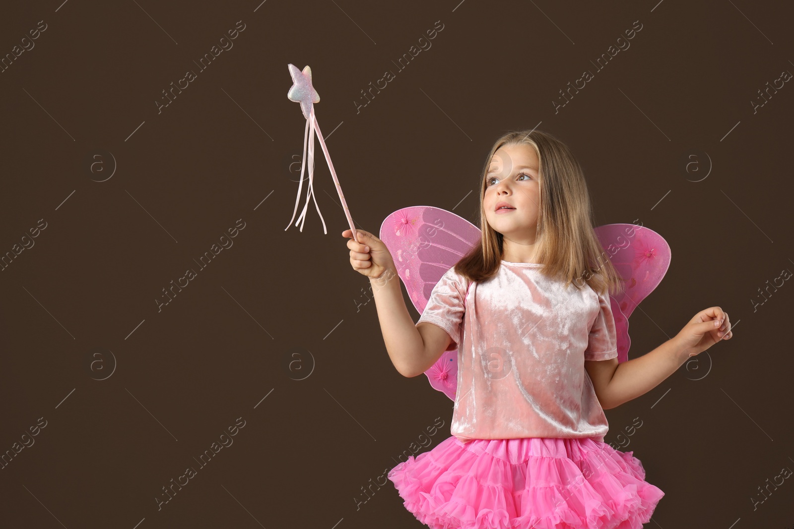 Photo of Cute little girl in fairy costume with wings and magic wand on brown background. Space for text