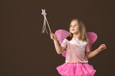 Photo of Cute little girl in fairy costume with wings and magic wand on brown background. Space for text