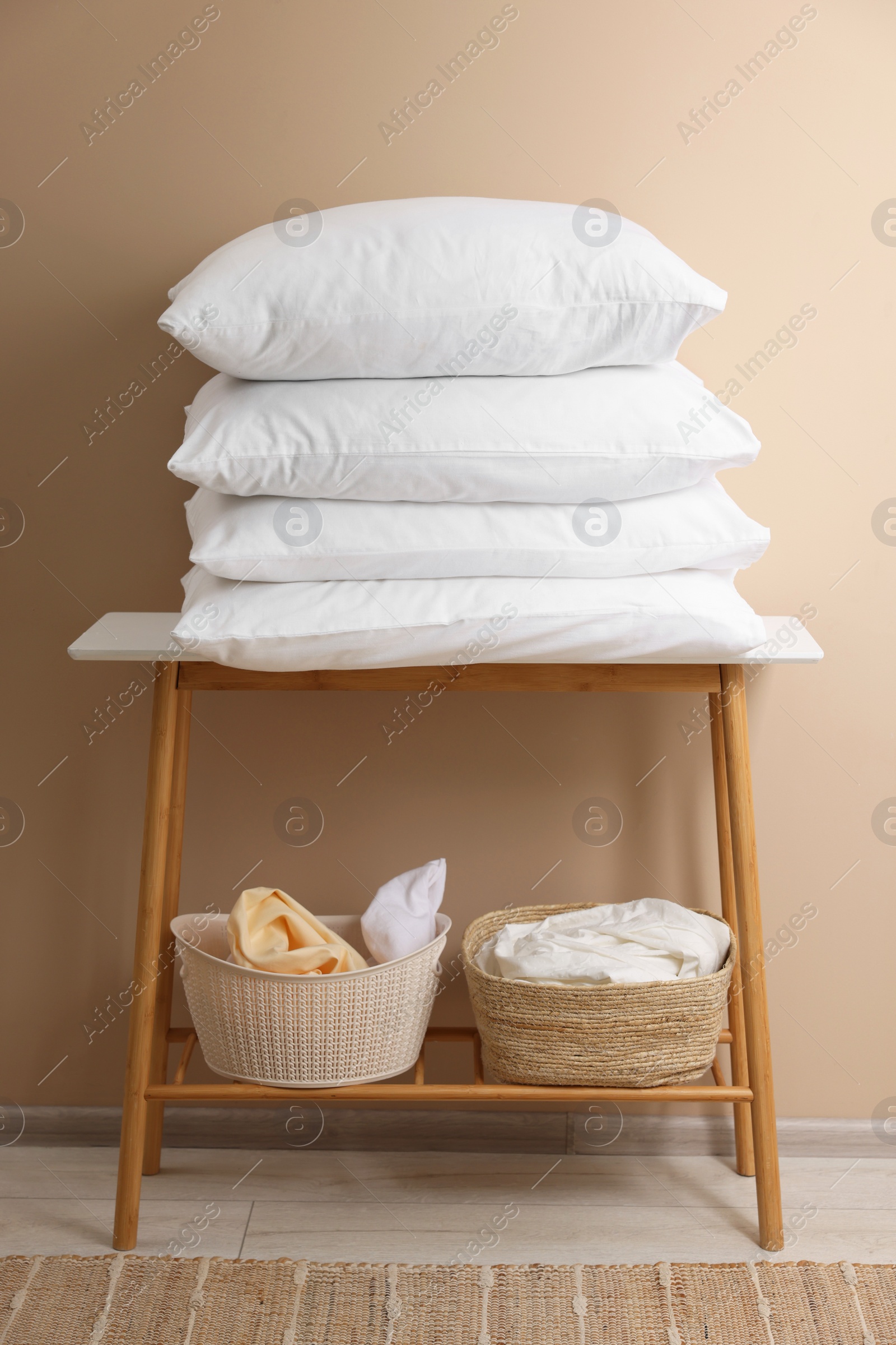 Photo of Stack of soft pillows and laundry baskets on table indoors