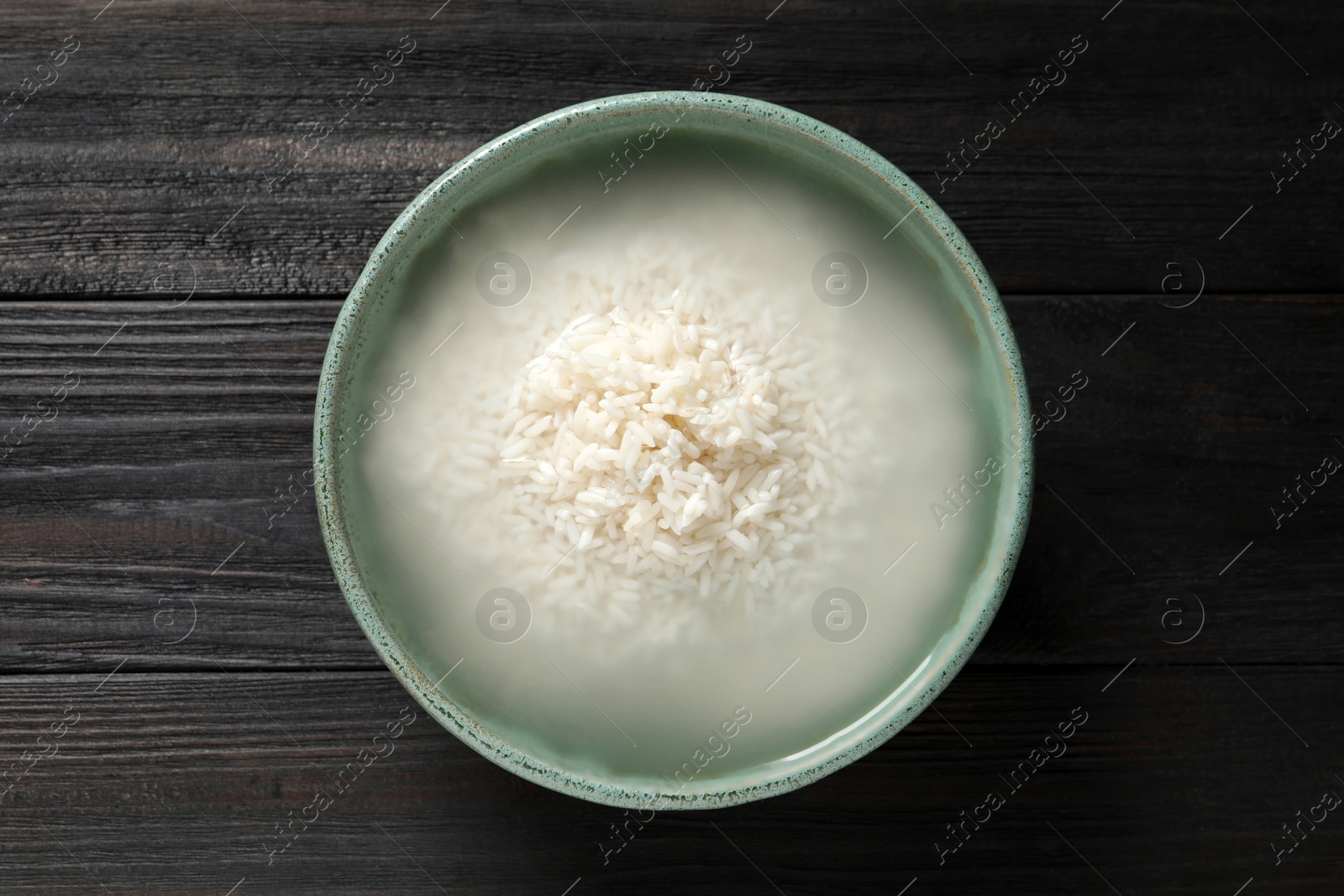 Photo of Bowl with rice soaked in water on black wooden table, top view