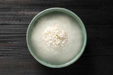 Photo of Bowl with rice soaked in water on black wooden table, top view