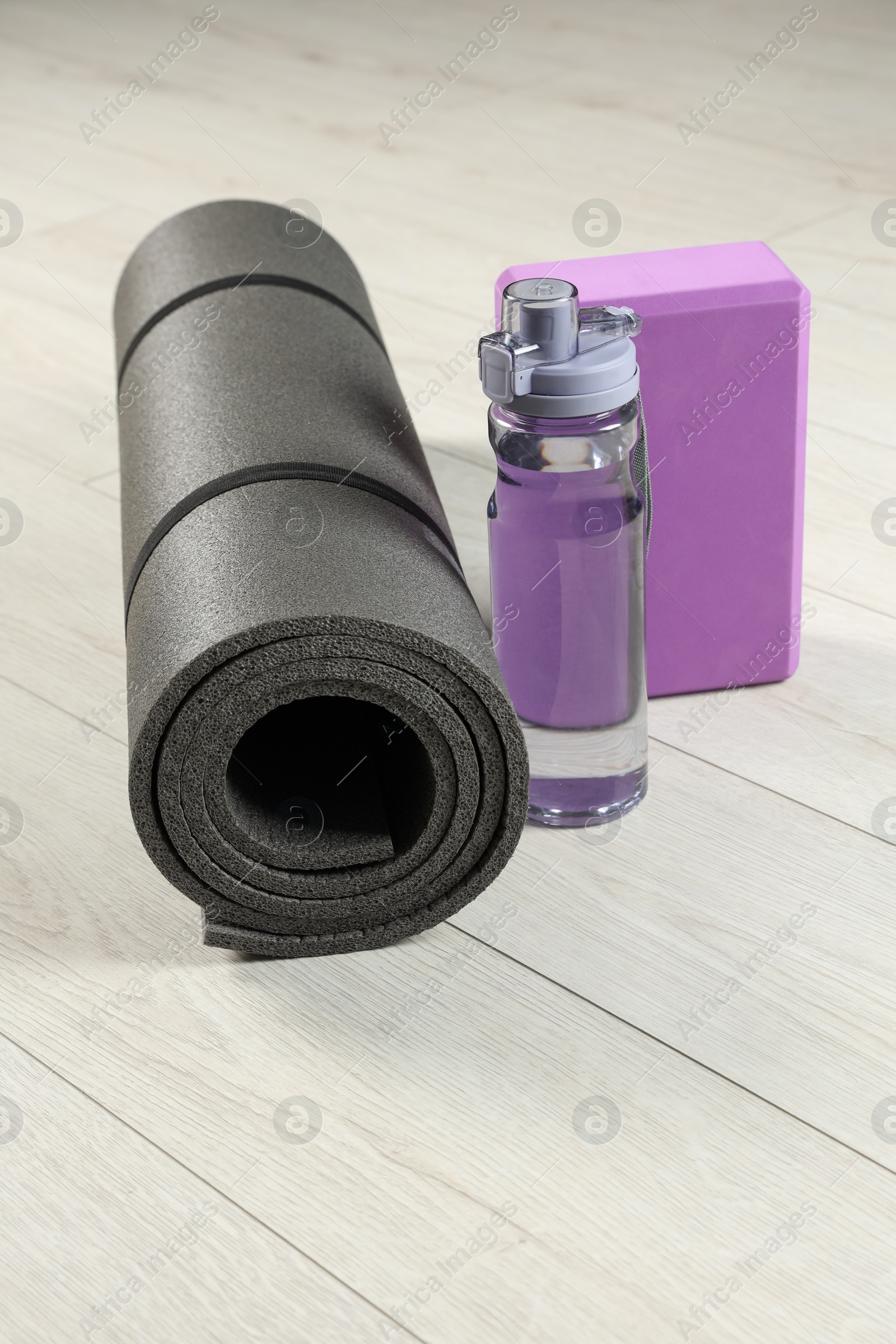 Photo of Exercise mat, yoga block and bottle of water on light wooden floor