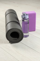 Photo of Exercise mat, yoga block and bottle of water on light wooden floor