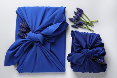 Photo of Furoshiki technique. Gifts packed in blue silk fabric and muscari flowers on white table, flat lay