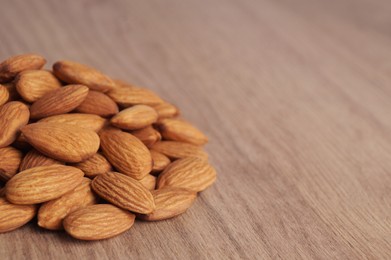 Pile of delicious almonds on wooden table, closeup. Space for text