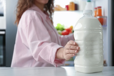 Young woman taking gallon of milk from table in kitchen, closeup