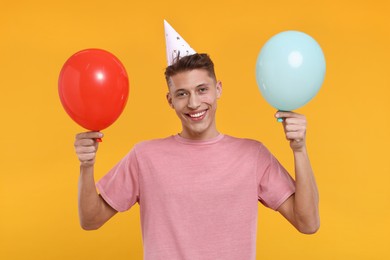 Photo of Happy man in party hat with balloons on orange background
