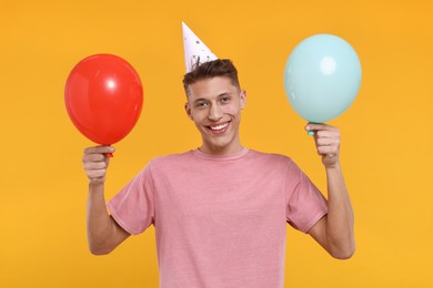 Happy man in party hat with balloons on orange background