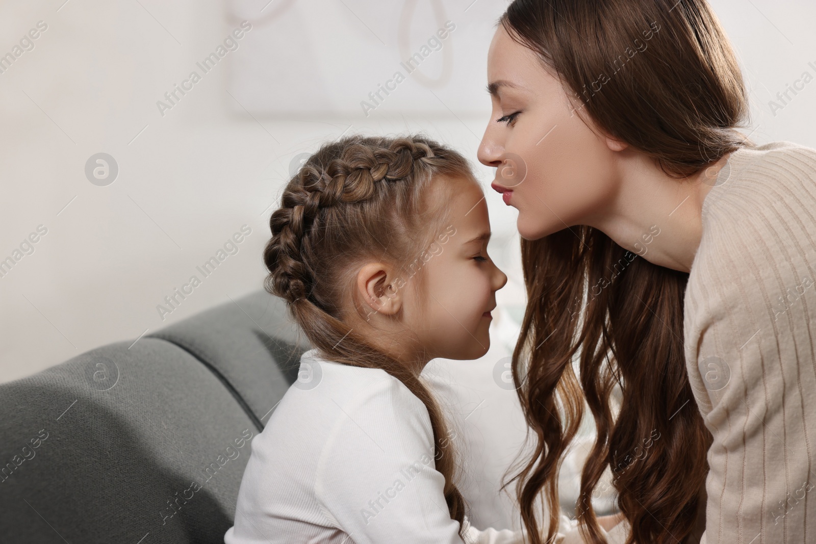 Photo of Happy mother kissing her cute daughter on sofa at home