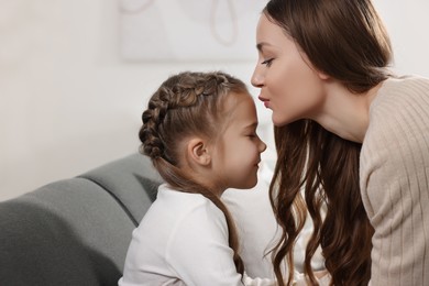 Happy mother kissing her cute daughter on sofa at home