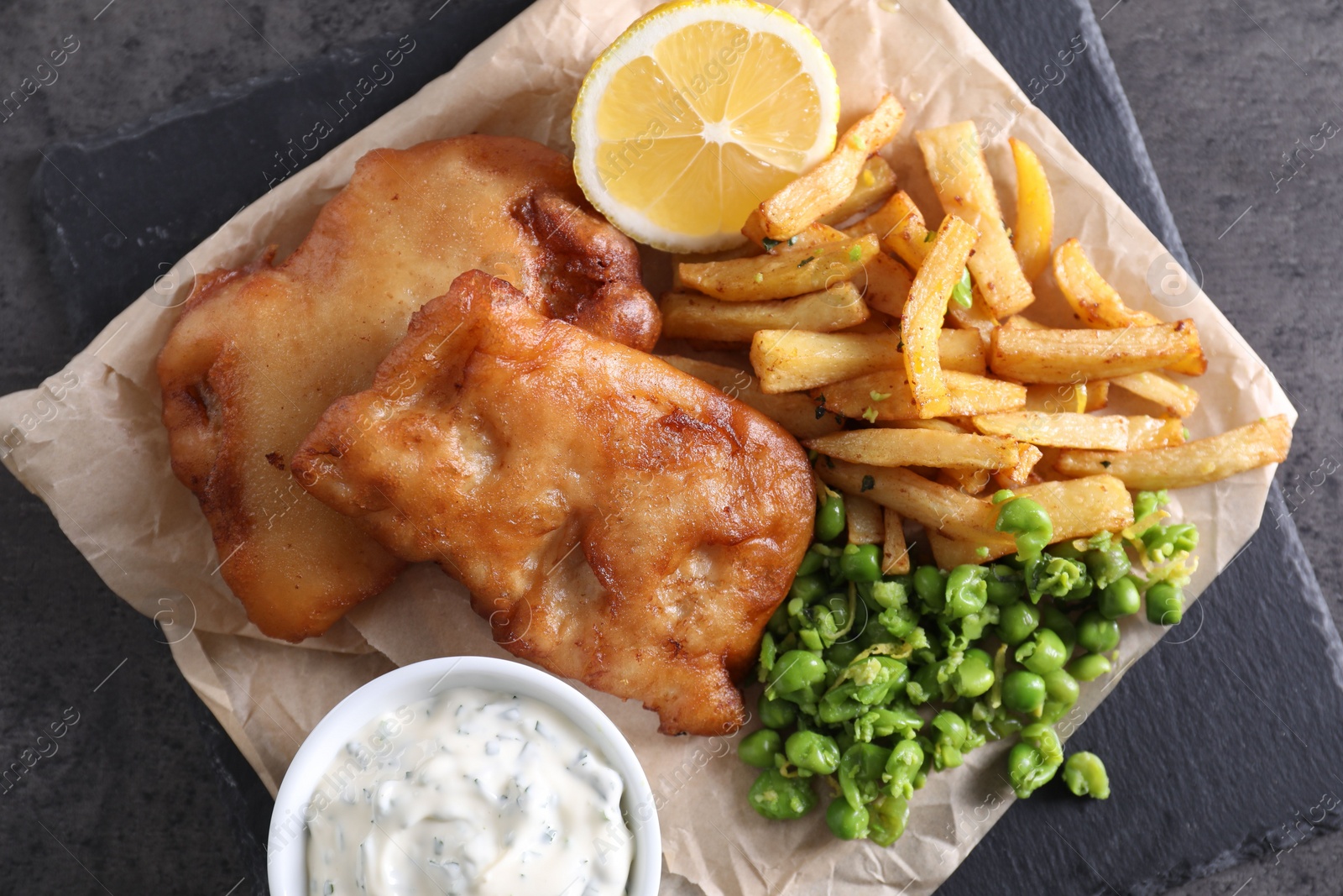 Photo of Tasty fish, chips, sauce and peas on grey table, top view