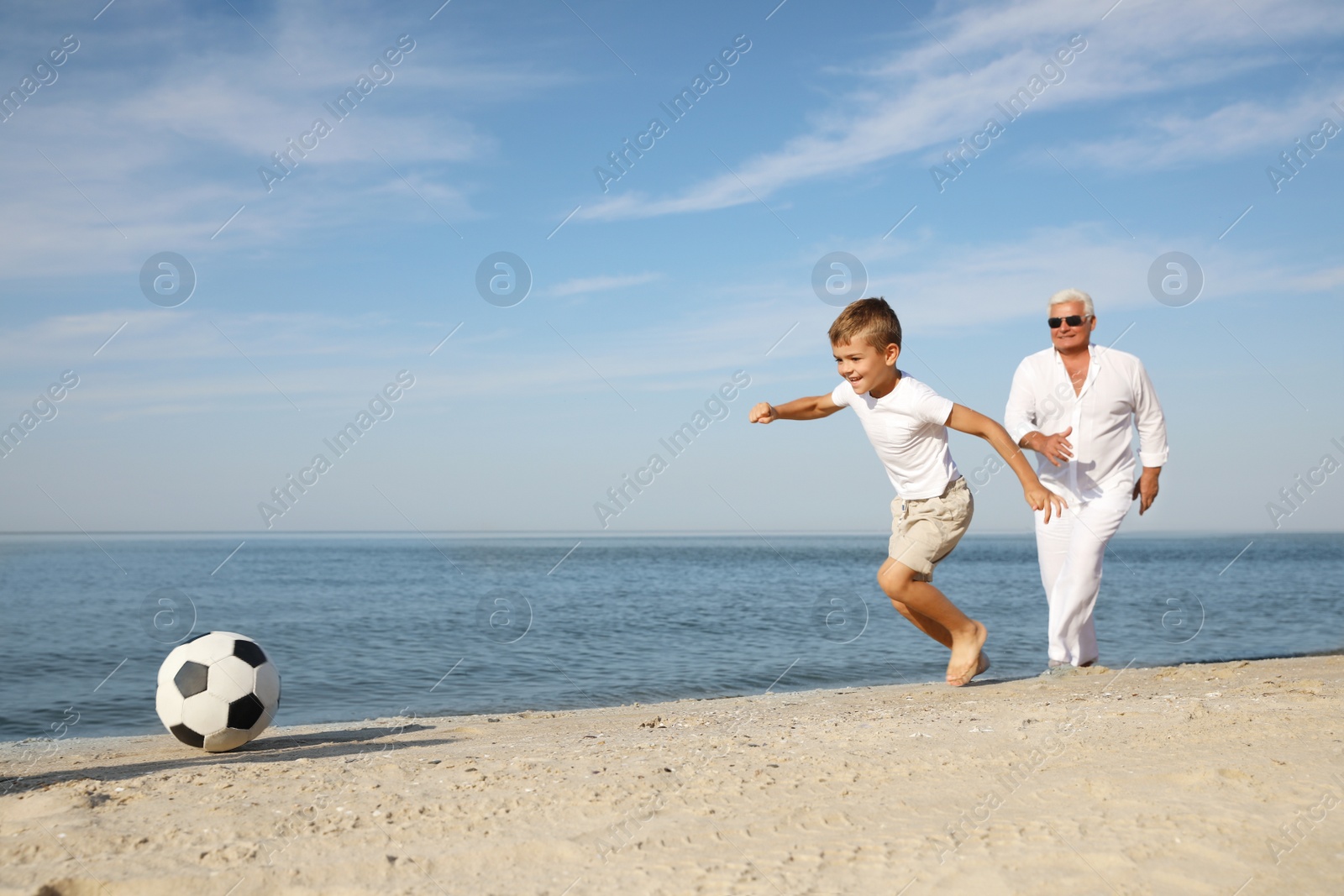 Photo of Cute little boy with grandfather playing football on sea beach